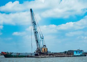 A crane barge stationed at a harbor under a partially cloudy sky, highlighting industrial maritime operations.