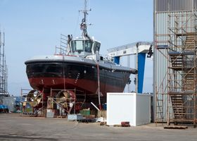 A large ship undergoing repairs in an industrial dockyard setting. Perfect for maritime industry themes.